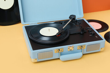 Record player with vinyl disks on table near orange wall