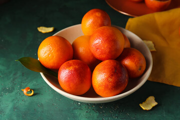 Bowl with tasty blood oranges on green background