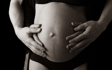 Closeup of naked round belly of pregnant mother in underwear held by mother and fathers hands. Last...