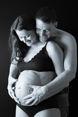 Smiling father and pregnant mother in underwear holding naked round belly. Last month of pregnancy...