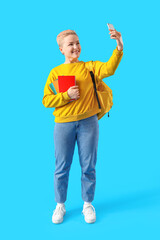 Female student with notebooks taking selfie on blue background