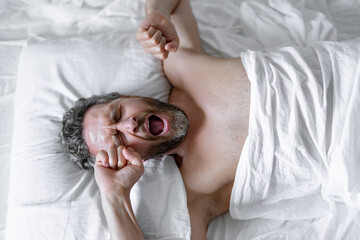 Man yawning waking up in white bed. Sexy shirtless man yawning in bed at bedroom. Hispanic mature man yawning at home at morning. Good sleep. Man yawning in bed. People wakeup.