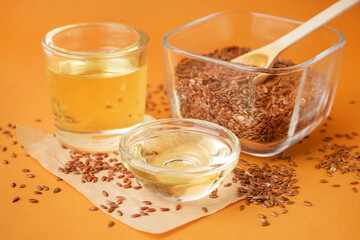 Glass with flax oil and bowl of seeds on orange background