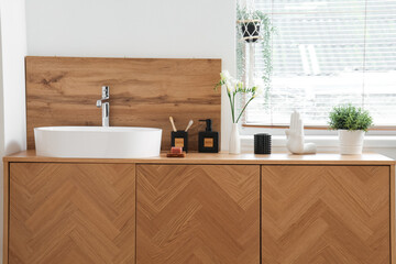 Sink, bath accessories and vase with flowers on table in room