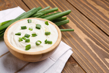 Bowl of tasty sour cream with green onion on wooden background