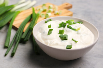 Bowl of tasty sour cream with green onion on grunge background
