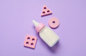 Bottle of milk for baby with toys on lilac background
