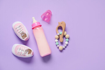 Bottle of milk for baby with rattle and booties on lilac background