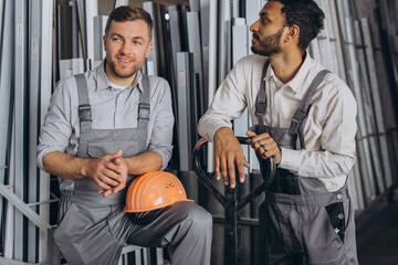 Portrait of two international workers wearing hardhats taking break from work and resting speaking to each other on a factory background with copy space