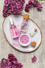 Fototapeta na wymiar Bottle of lilac essential oil, sea salt and flowers on grunge background