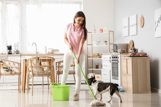 Young woman with her French bulldog mopping floor in kitchen