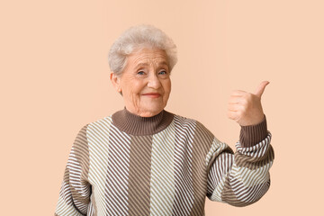Senior woman showing thumb-up on beige background