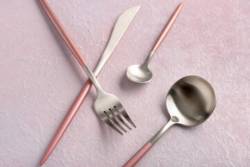 Stainless steel cutlery with pink handles on lilac background