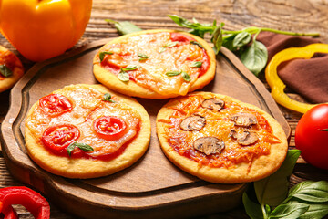Board with different tasty mini pizzas on wooden background