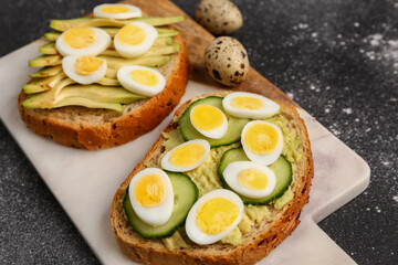 Tasty toasts with quail eggs, avocado and cucumber on dark grunge background, closeup