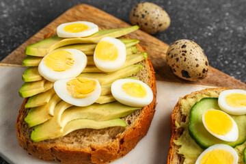 Tasty toasts with quail eggs, avocado and cucumber on dark grunge background, closeup
