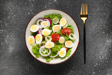 Tasty salad with quail eggs, tomatoes, onion and lettuce on dark grunge background
