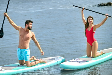 Couple of tourists young man and woman having fun paddleboarding at sea, enjoying summer vacation.