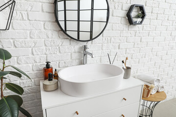 Mirror, sink bowl and bath accessories on chest of drawers in bathroom