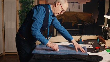 Senior couturier fabricating material to design custom made fashion items, needlework concept. Small buisness owner manufacturing clothes with professional fabric in tailor workshop.
