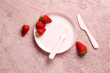 Plate with eating utensils for baby and fresh strawberry on grunge pink background