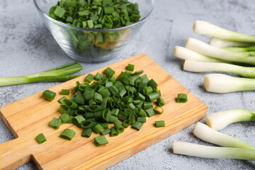 Board and bowl with slices of fresh green onion on grey background