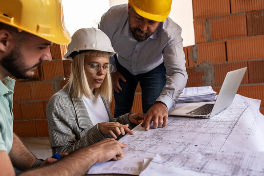 A female architect and a focused construction managers engage in an animated discussion, analyzing blueprints.