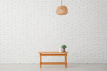 Wooden table with bonsai tree and decorative figure near white brick wall