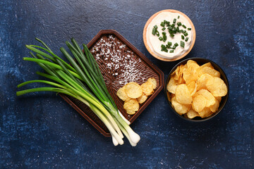 Bowl of tasty sour cream with sliced green onion and potato chips on blue background