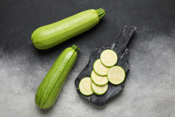Board with slices of fresh green zucchini on grey background