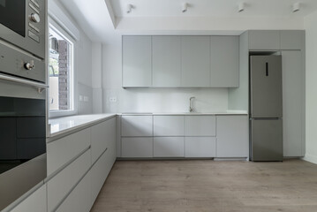 Newly installed modern kitchen covering two walls in an L shape with gray cabinets, white stone countertops