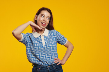 Portrait of a happy young girl looking at free empty space while sticking her tongue out isolated over yellow background