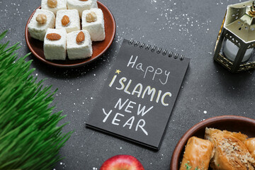 Fototapeta na wymiar Notebook with text HAPPY ISLAMIC NEW YEAR, sweets and fanous on dark background, closeup