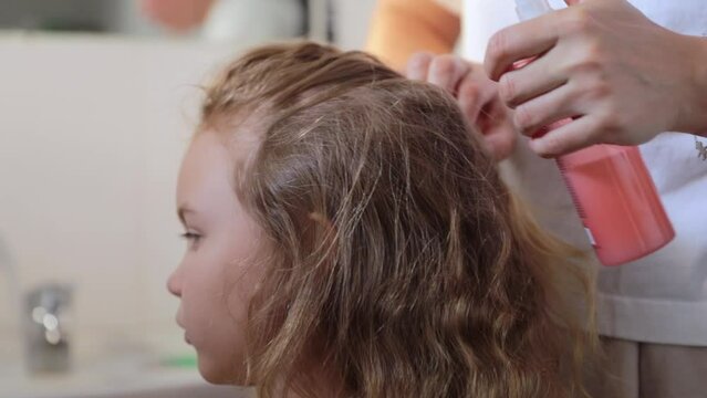 Women's hands apply a remedy for lice and nits on the head of a little girl. Getting rid of parasites and pests, childhood diseases.