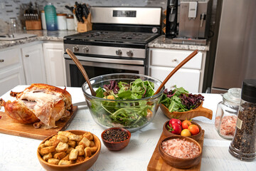 Freshly prepared Caesar salad in a glass bowl is on the kitchen table. Grilled chicken, crackers and ingredients.