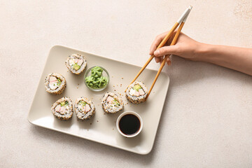 Hand of woman eating tasty sushi rolls at light table, top view