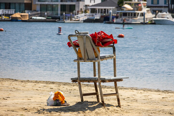 a rusty metal chair in the sand at Horny Corner Beach with a red umbrella on top, blue ocean water, people on paddle boats with boats and yachts along the banks in Long Beach California USA