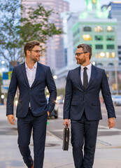 Businessmen communicating at meeting. Two businessmen discussing outdoor during business meeting. Businessmen talking. Business partners walking outdoor. 40s businessman walking by street.