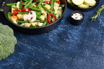 Frying pan with fresh vegetables on blue background
