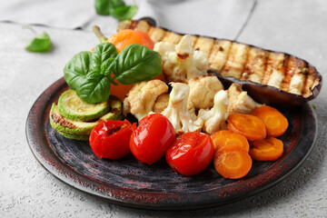 Plate with grilled vegetables and basil on grey background