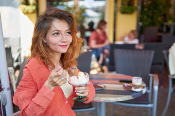 Closeup portrait of a beautiful   woman enjoy eating an ice cream in outdoor restaurant in Europe. Tourist woman in a cafe enjoying her desert cake ice cream                              at outdoor.