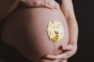 Baby bump shot with glittering lion sticker from the side of pregnant woman holding the belly at...