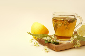 Board with glass cup of linden tea and lemon on beige background