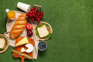 Composition with tasty food, juice and sandwiches for picnic on green background