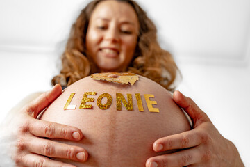 Baby bump shot with glittering lion sticker and child name from below of laughing pregnant woman at...