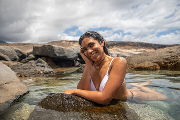 A happy woman bathes by the sea in a crystalline pond, summertime relaxation