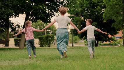 Mother child son, daughter playing, running on green grass, holding hands, park. Happy running children boy girl, mom in nature. Weekend with family. Family walks outdoors in summer. Family Teamwork