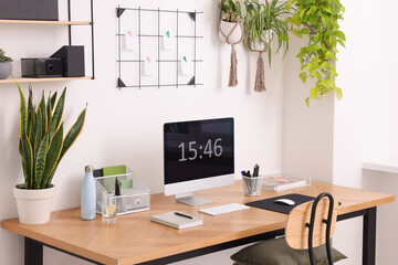 Cozy workplace with computer, modern furniture and houseplants at home