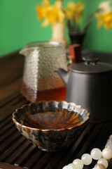 Cup with freshly brewed pu-erh tea and prayer beads on wooden tray, closeup