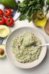 Delicious guacamole in bowl and ingredients on white wooden table, flat lay